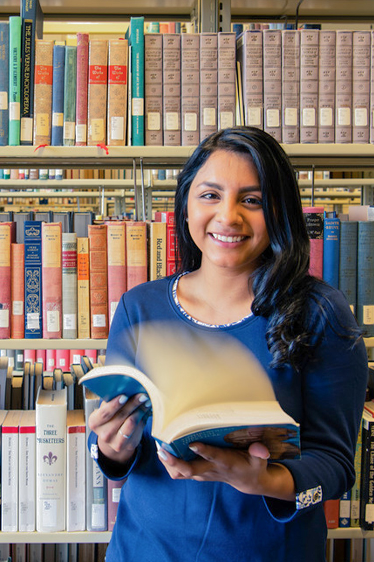 girl standing in library flipping through book